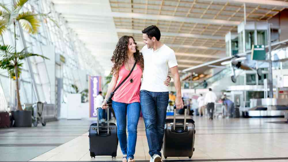 A relaxed man and woman smiling while walking through an airport with carry-on luggage