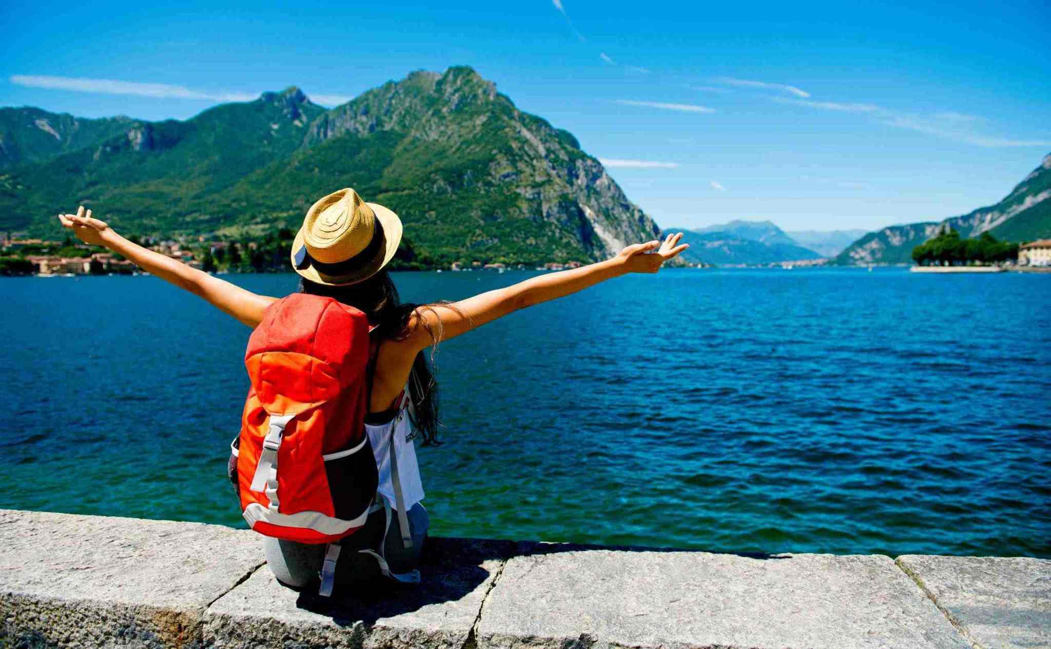 A woman standing by a beautiful mountain lake with her arms outstretched in freedom