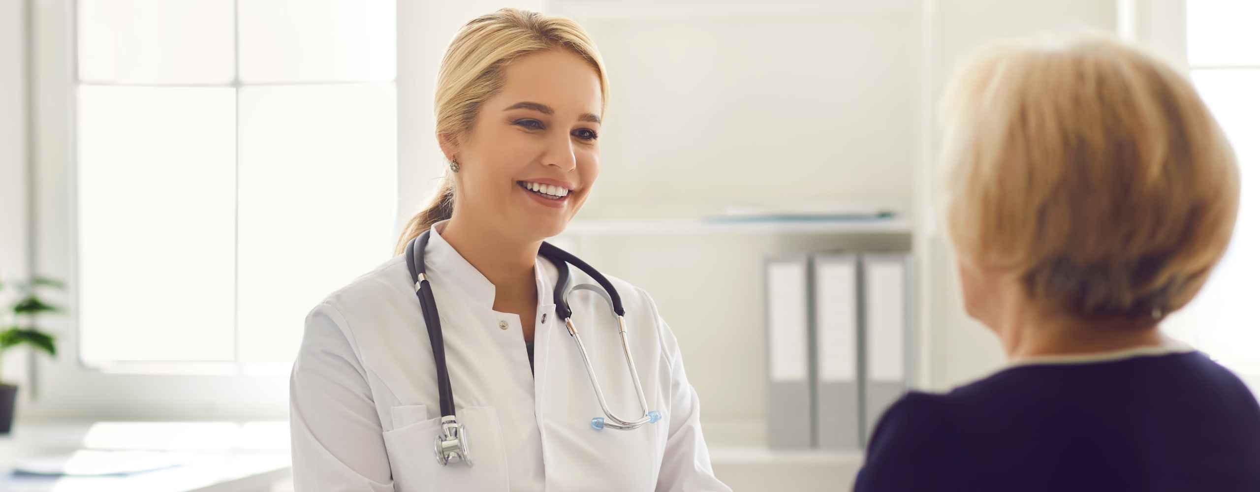 A smiling female doctor wearing a white lab coat and stethoscope consulting with a female patient.