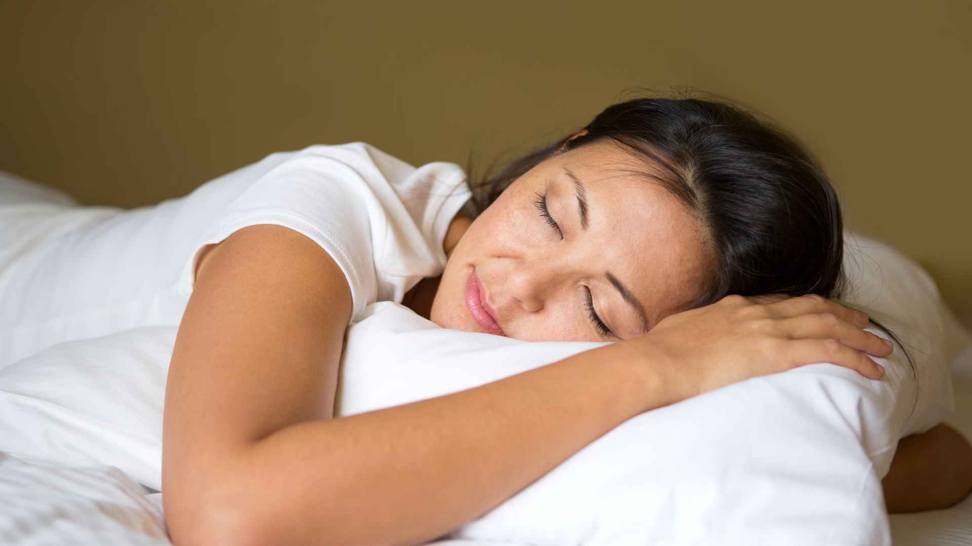 A woman is sleeping peacefully in bed, a small contented smile on her face.