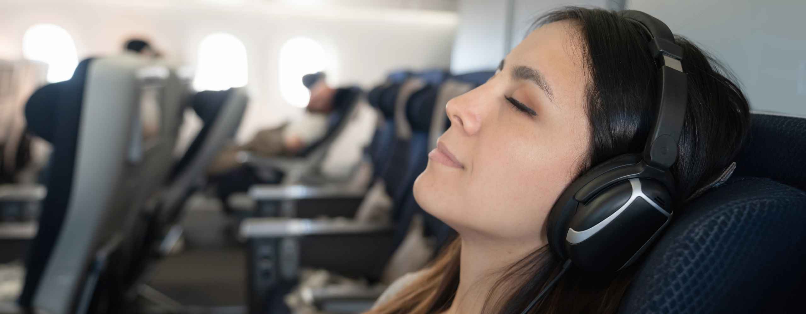 A woman wearing headphones sleeps peacefully in a plane seat, illustrating a calm and relaxed flight experience