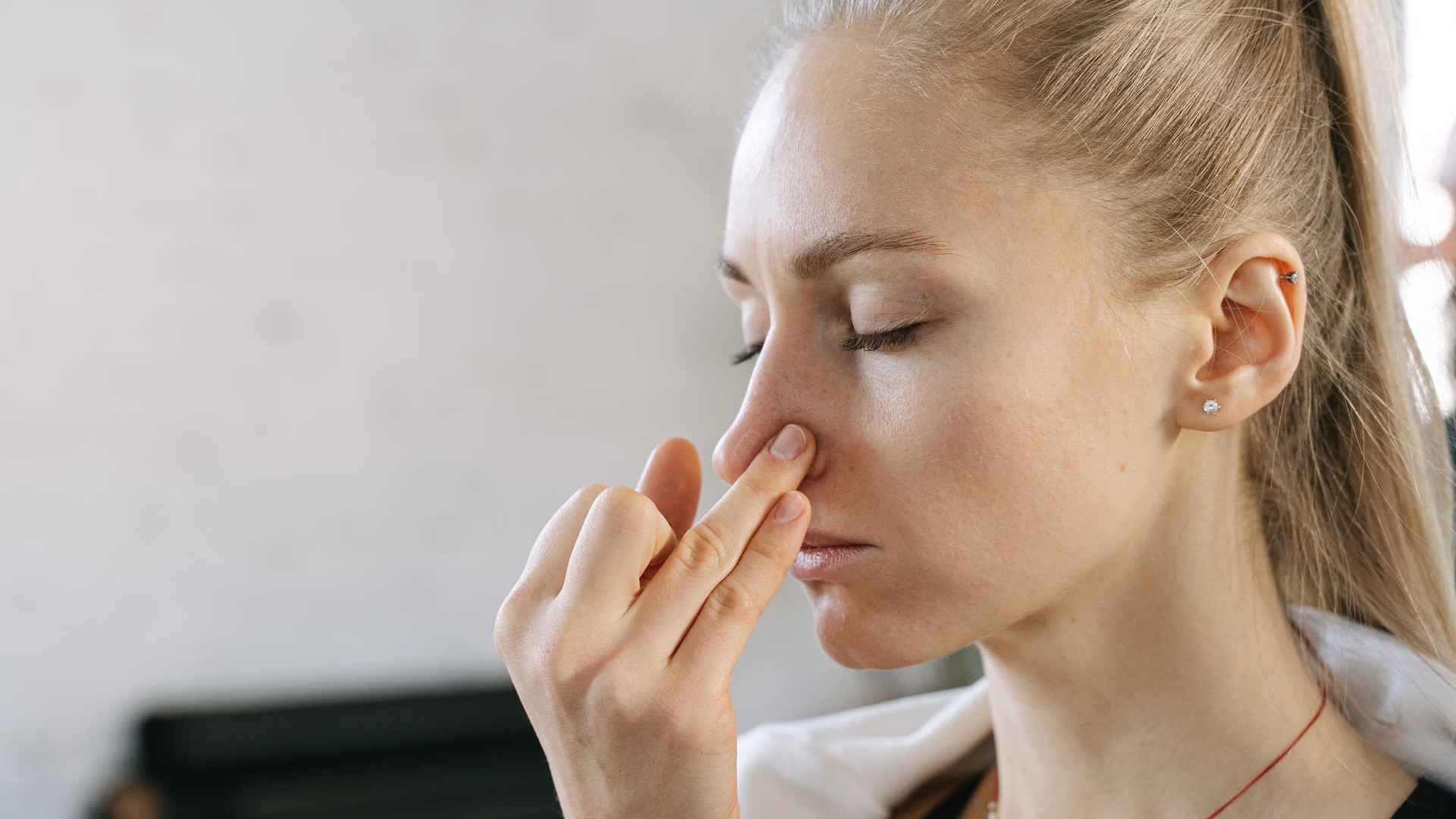 A woman with her eyes closed, practicing alternate nostril breathing. She is using the fourth finger on her right hand to close her left nostril.
