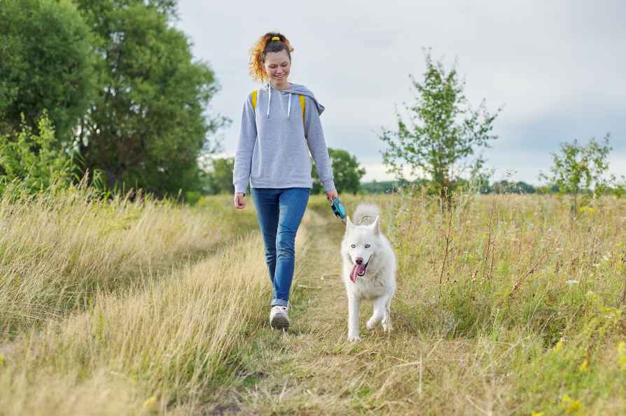 A woman wearing jeans and a hoodie, walking her dog in the park on a sunny day, with a calm and happy expression